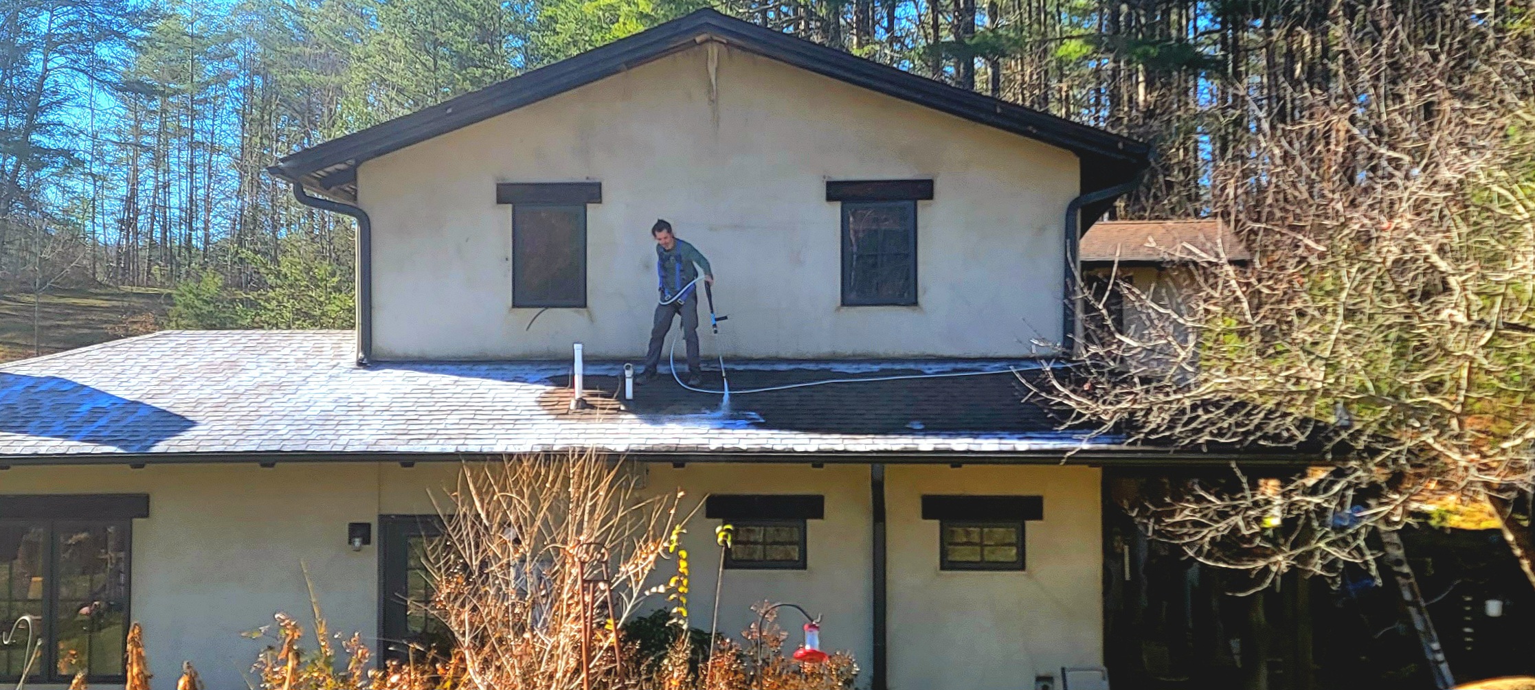 man on roof for rural home. spraying roof restoration solution. two story house in the forest of wnc